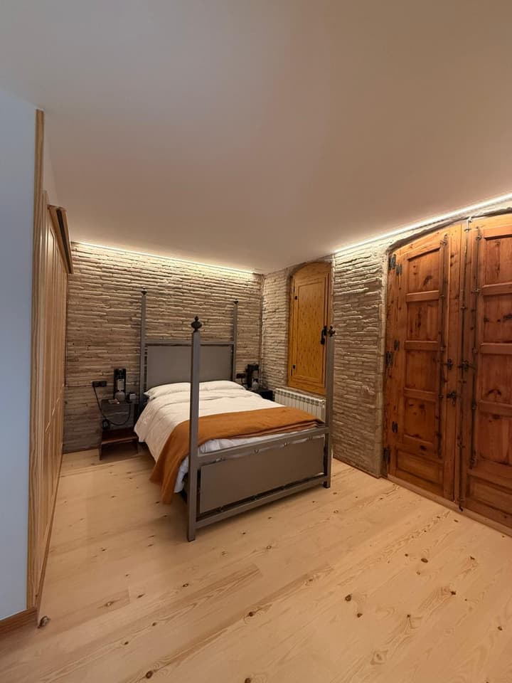 Dormitorio reformado con muro de piedra vista, cama con dosel de forja e iluminación LED