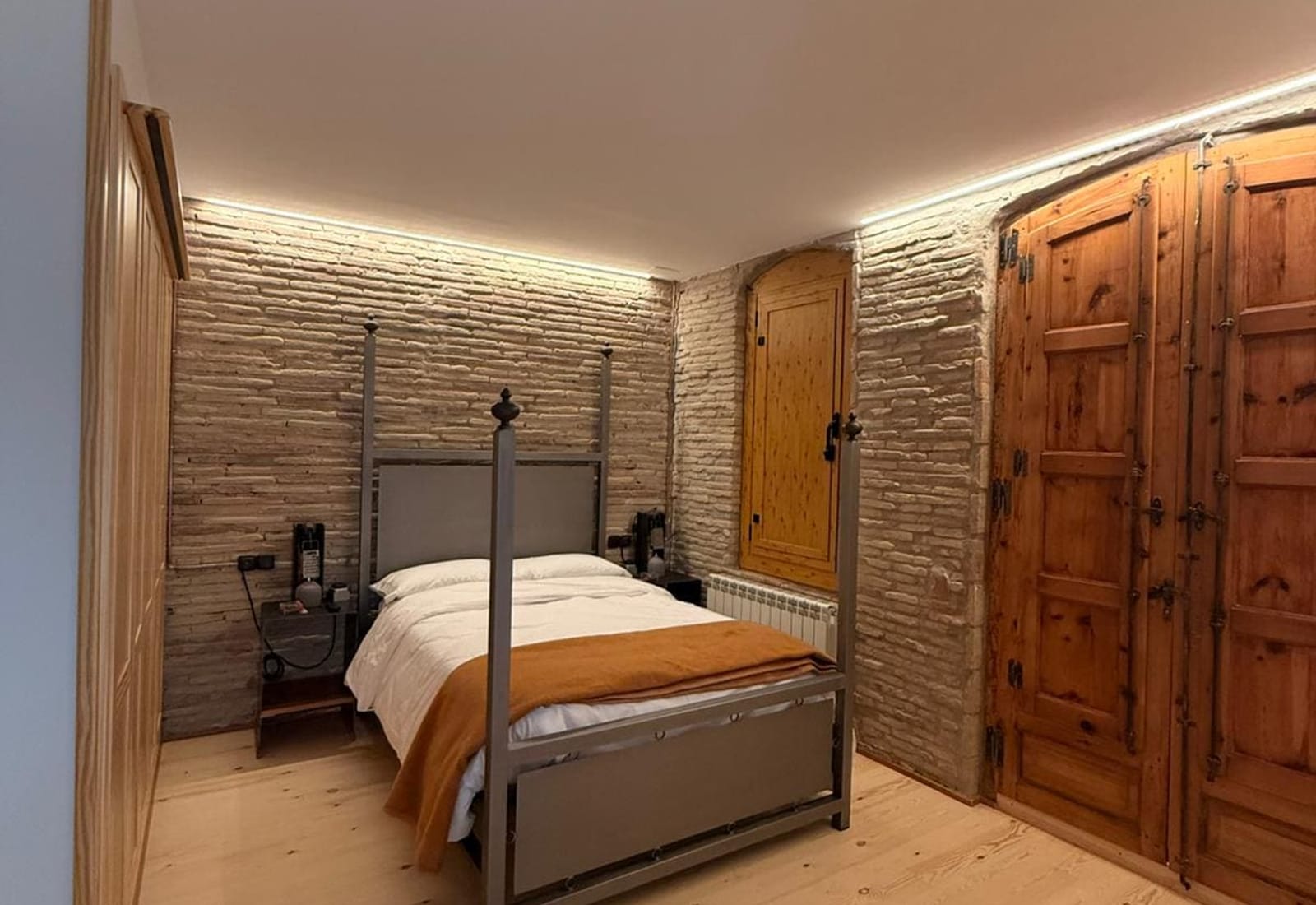 Dormitorio reformado por JIMA con pared de piedra, cama de forja y puertas antiguas restauradas